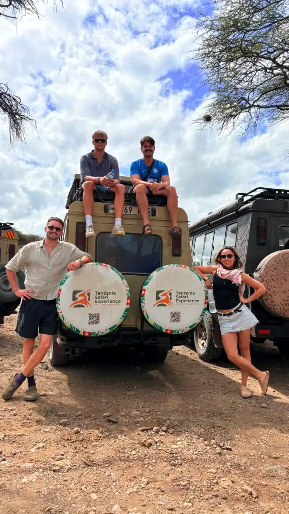 Travelers posing beside a Tanzania Safari Experience safari vehicle during a Serengeti safari adventure in Tanzania.
