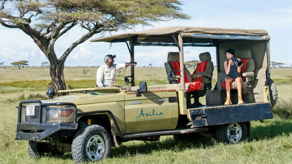 Which is the best Safari Operator in Tanzania? Private safari game drive in the Serengeti with a guide and photographer in an open-sided 4x4 Land Cruiser overlooking the African savannah.