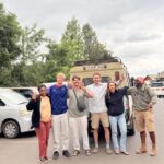 Safari guests posing with their guide beside a Tanzania safari vehicle after a game drive.