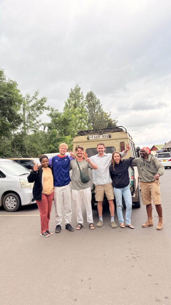 Safari guests posing with their guide beside a Tanzania safari vehicle after a game drive.